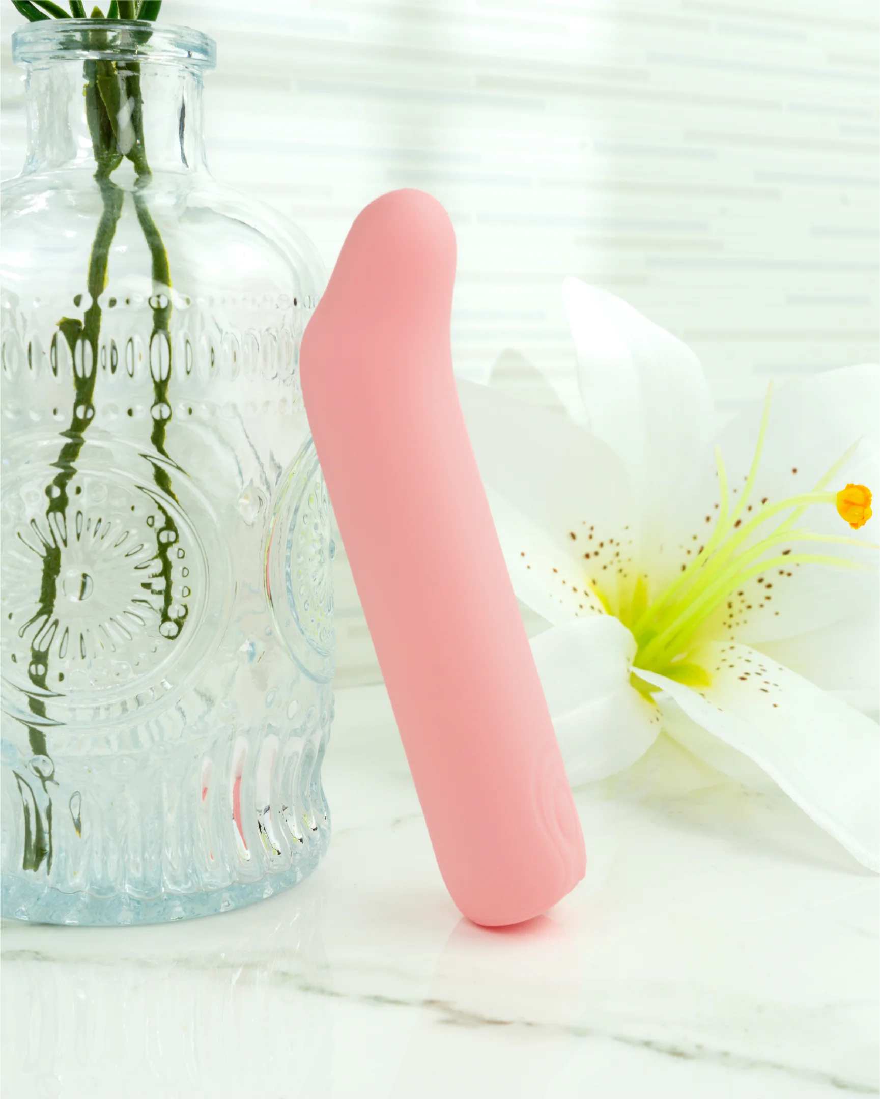 Pastel pink Blush & Bloom Iris curved mini G-spot vibrator displayed on marble surface with soft floral background