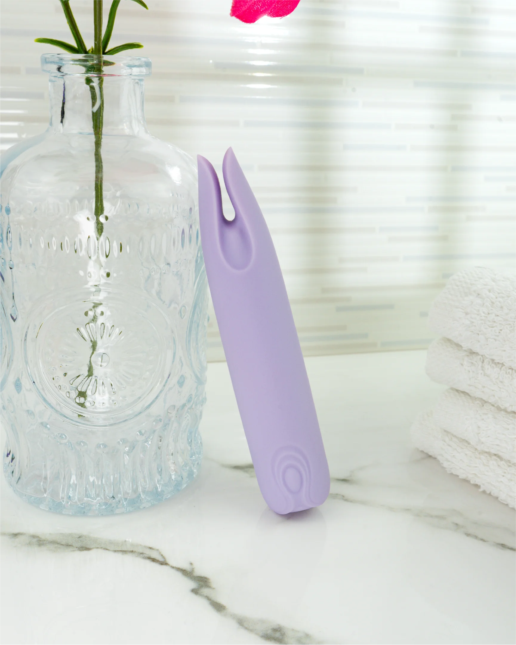 Pastel purple Blush & Bloom Petunia mini vibrator beside glass bottle on marble surface, waterproof dual-tip clitoral vibrator