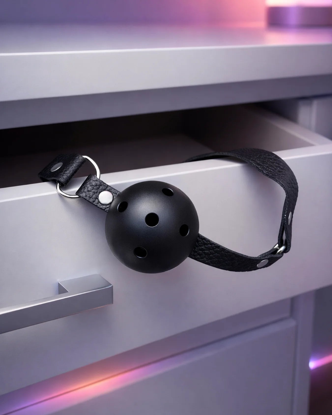 Black breathable ball gag with airflow holes shown in bedroom setting for secure and low-strain mouth restraint