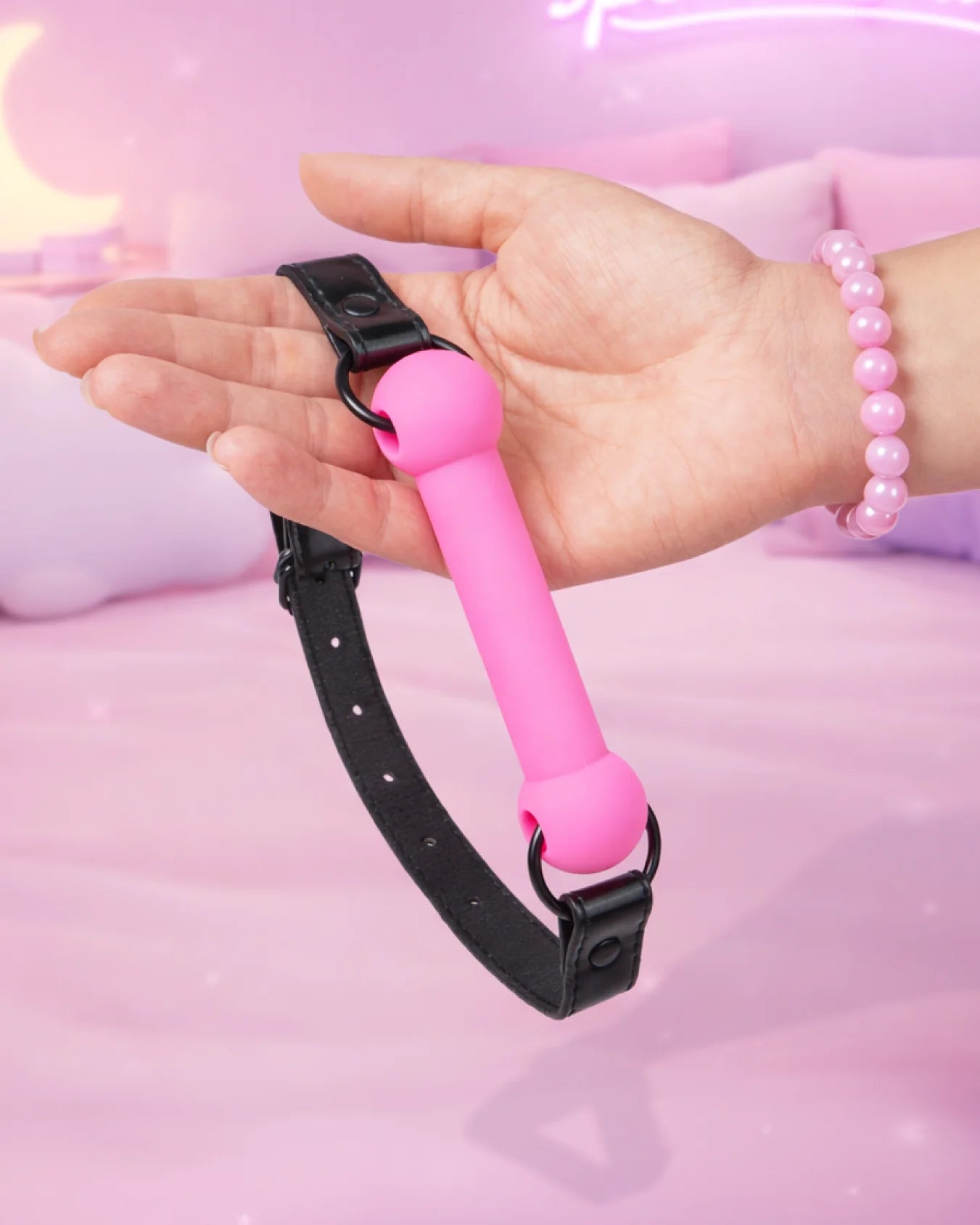 Pink silicone bit gag held in hand showing size and flexible strap, comfortable beginner mouth gag design