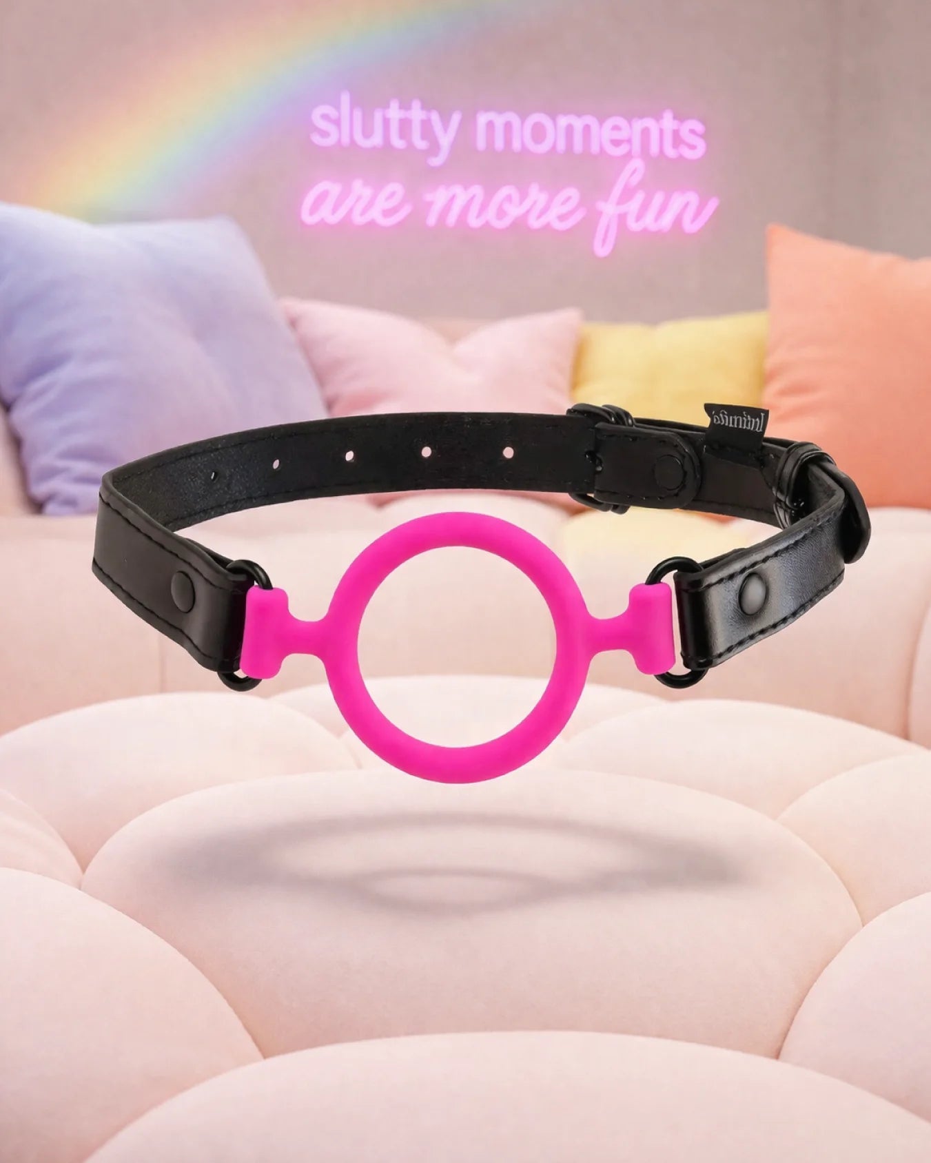 Pink silicone O-ring gag by Empower Play™ floating in soft bedroom setting, open-mouth design for breathable mouth restraint