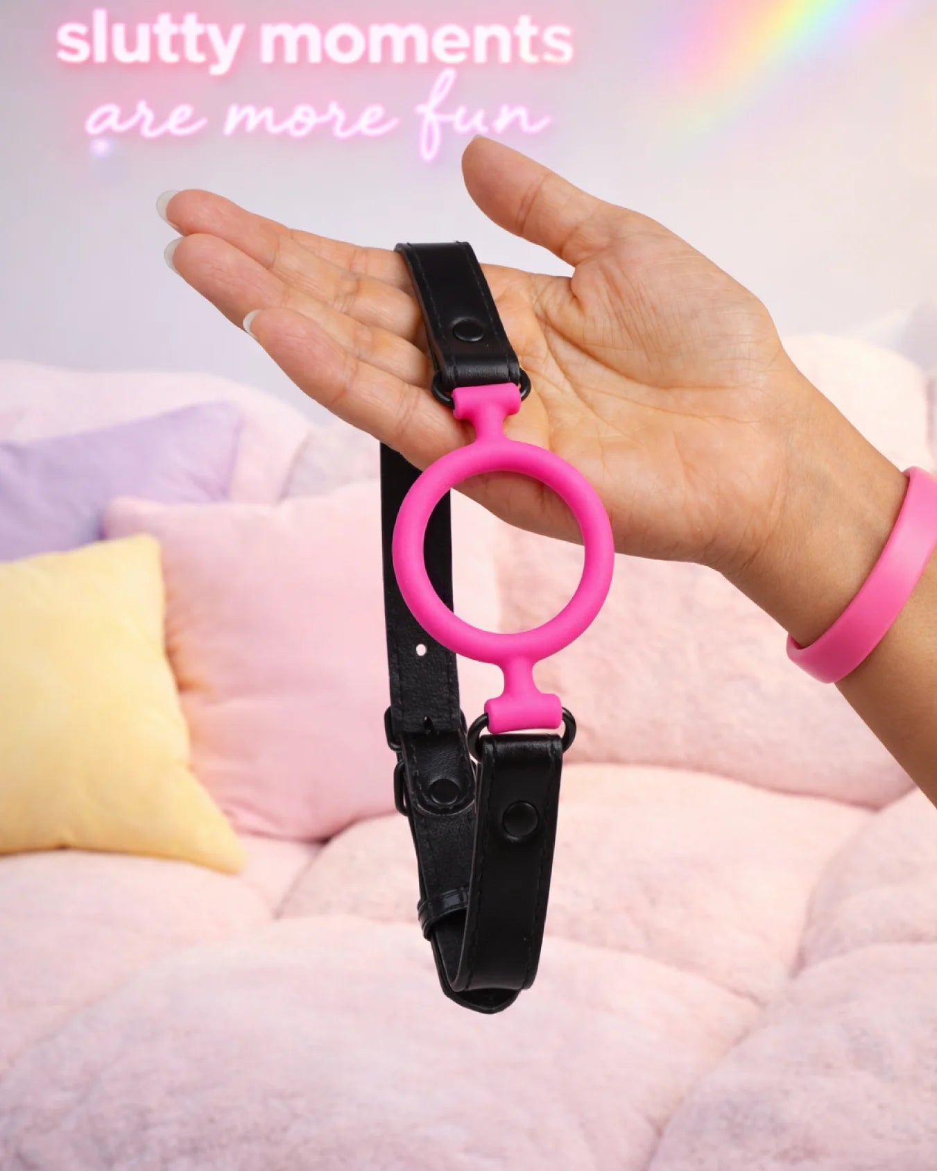 Pink silicone O-ring gag held in hand showing size, open-mouth ring design, and adjustable strap for comfortable fit