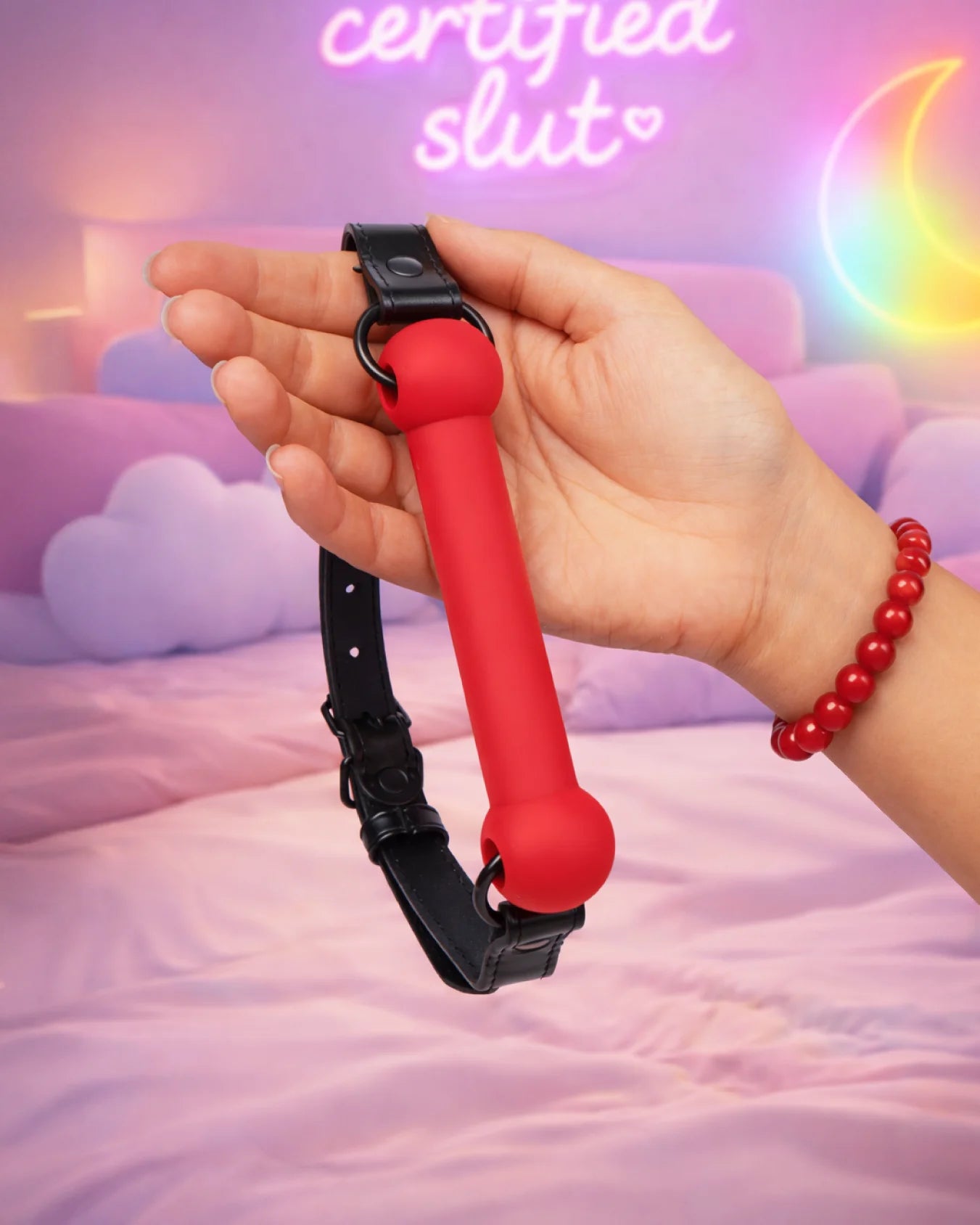 Red silicone bit gag held in hand showing scale, soft texture, and adjustable strap design