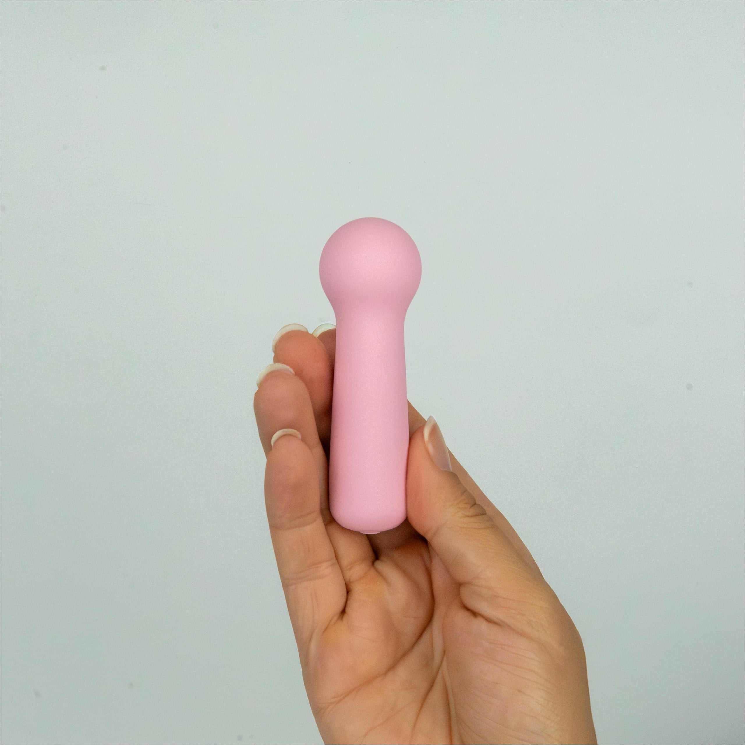 Joy Penny mini wand clitoral massager in pastel pink shown in hand to demonstrate compact size and easy grip
