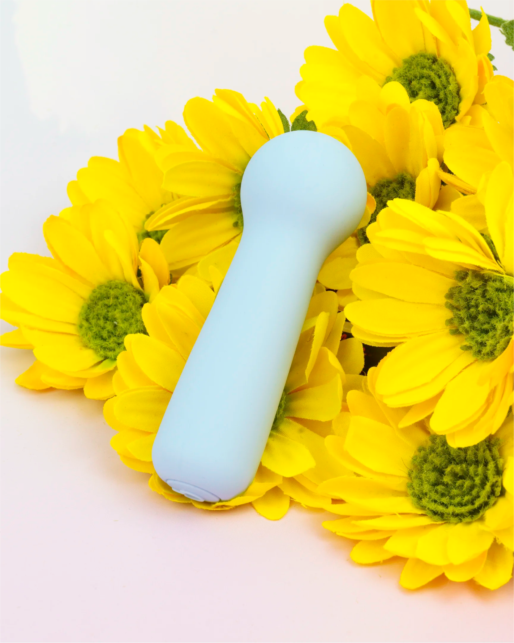 Pastel blue Joy Penny mini wand vibrator with rounded head displayed with flowers, compact waterproof design made from silky body-safe silicone