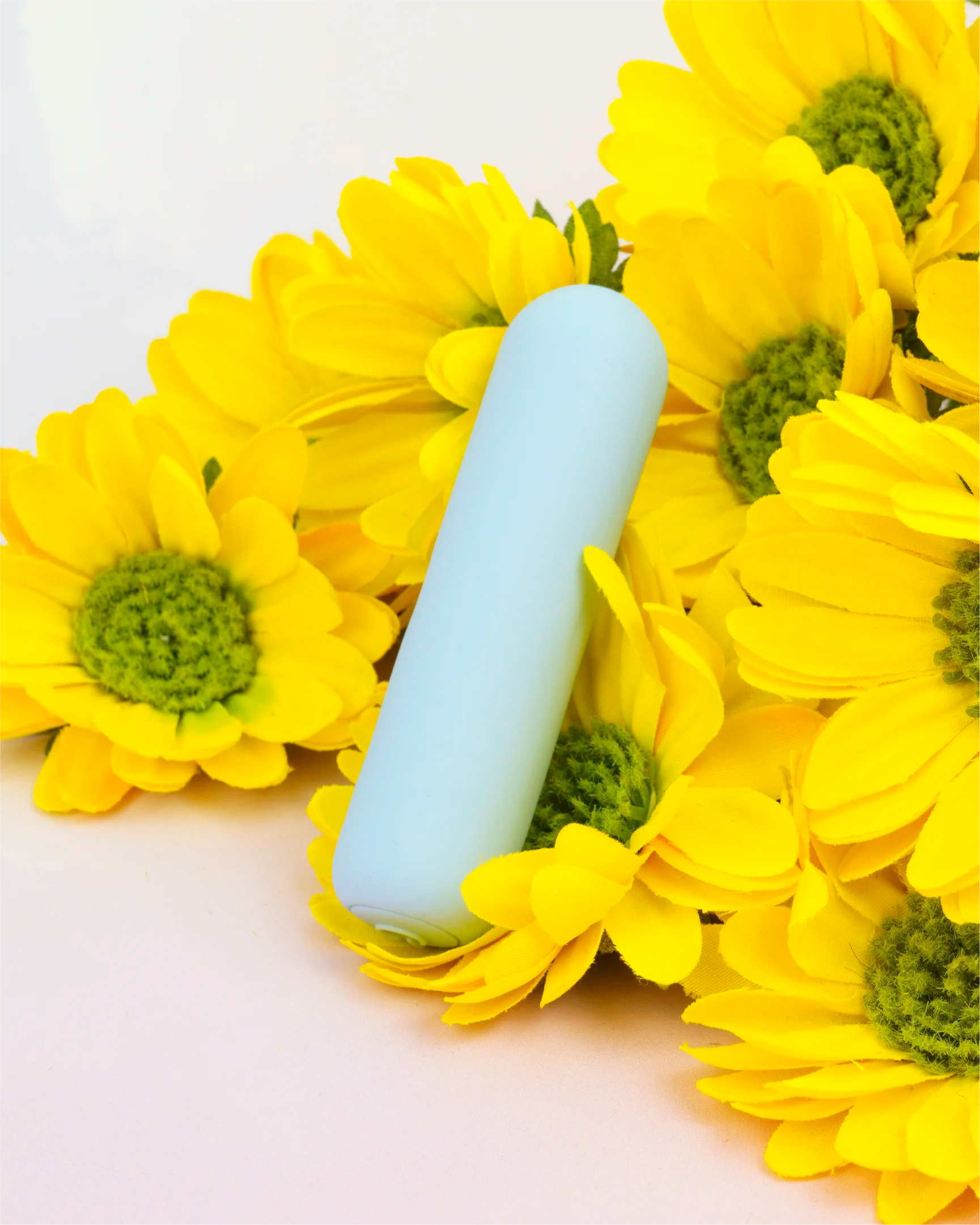 Pastel blue Joy Pippa rechargeable bullet vibrator displayed with bright flowers, compact waterproof design made from silky body-safe silicone