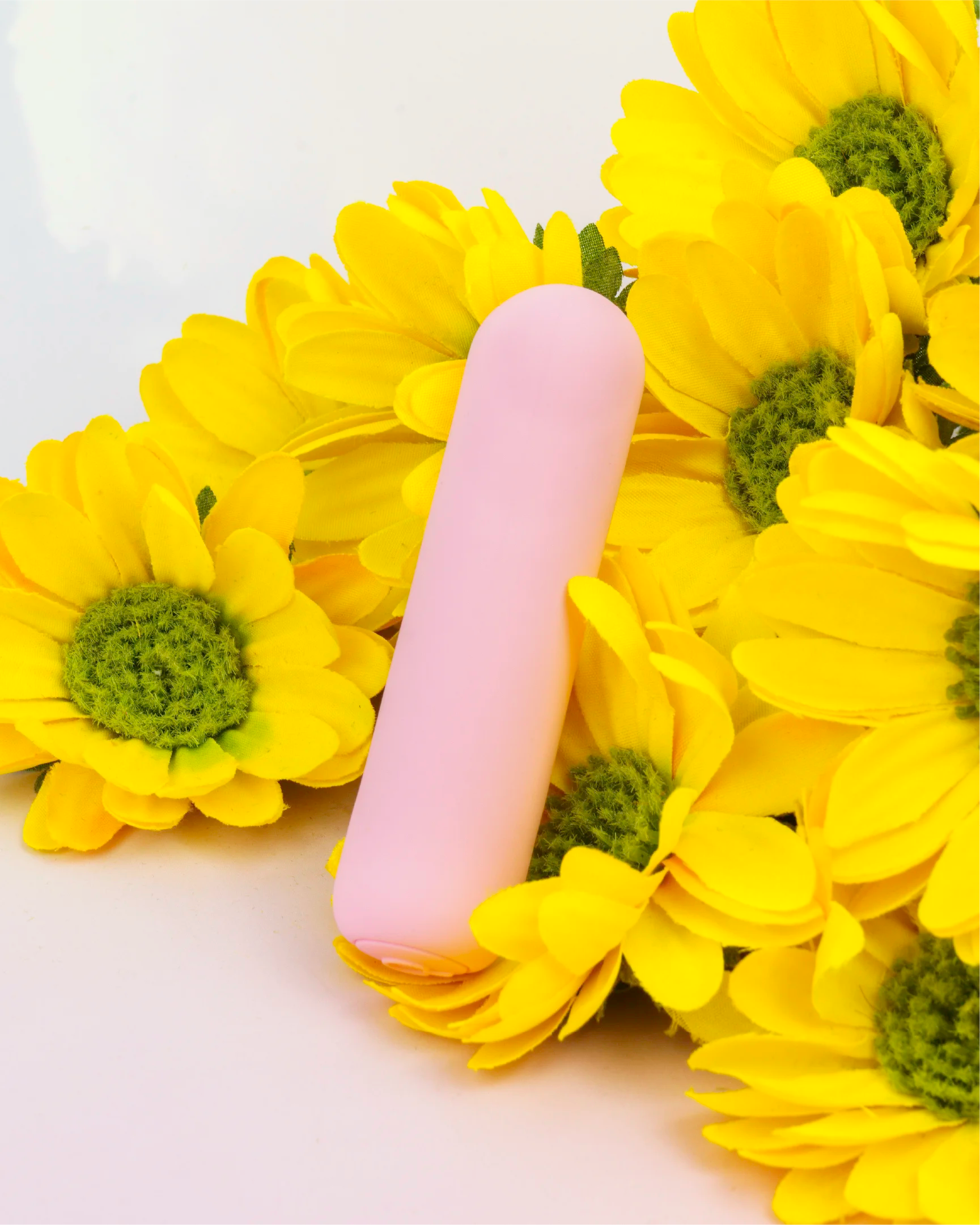 Pastel pink Joy Pippa rechargeable bullet vibrator displayed with yellow flowers, compact waterproof design made from silky smooth body-safe silicone