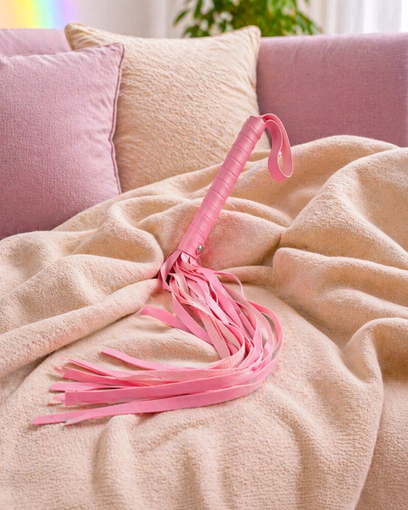 Pink faux leather BDSM flogger resting on bed with soft tails for beginner-friendly impact and sensation play