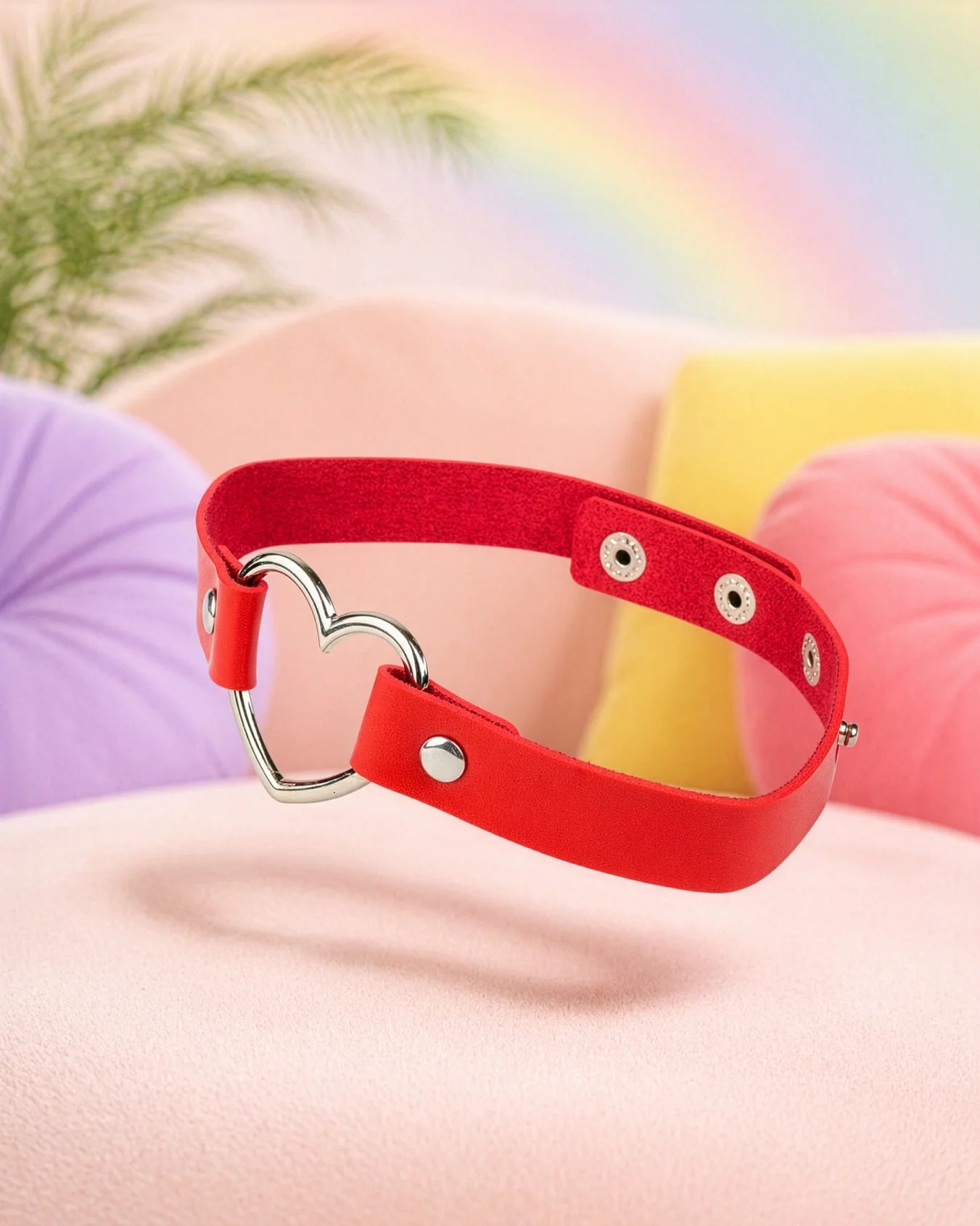 Red faux leather heart choker collar floating in soft bedroom setting, bold BDSM collar with adjustable fit and metal heart ring
